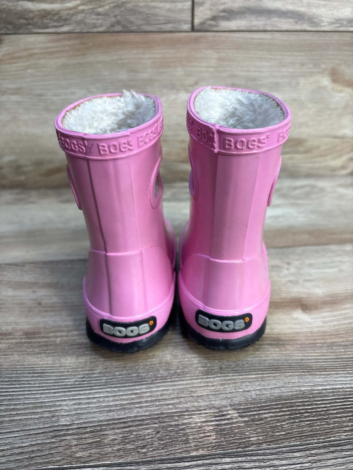 Pink Bogs kids rain boots with plush lining, shown on a wood floor