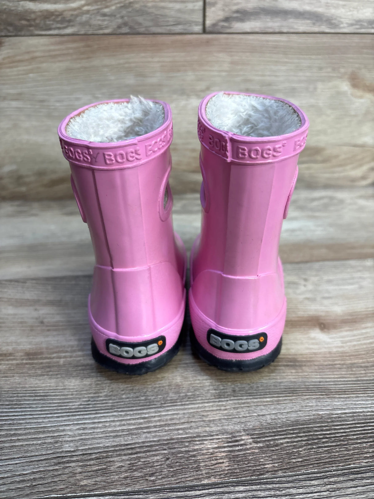Pink Bogs kids rain boots with plush lining, shown on a wood floor