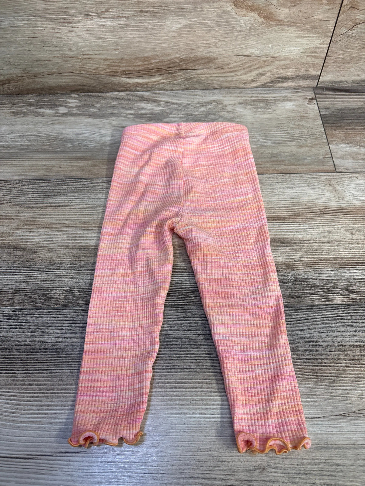 Front view of Old Navy ribbed leggings showcasing orange ribbed fabric and ruffled hems on a wood floor