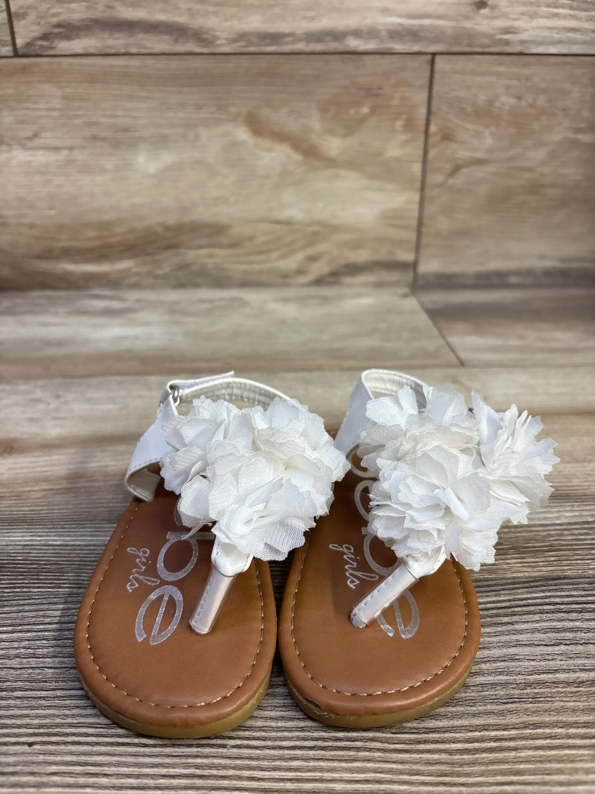 Front view of Bebe chiffon flower sandals in white, size 7C showcasing chiffon flower accents with a wood-look floor background