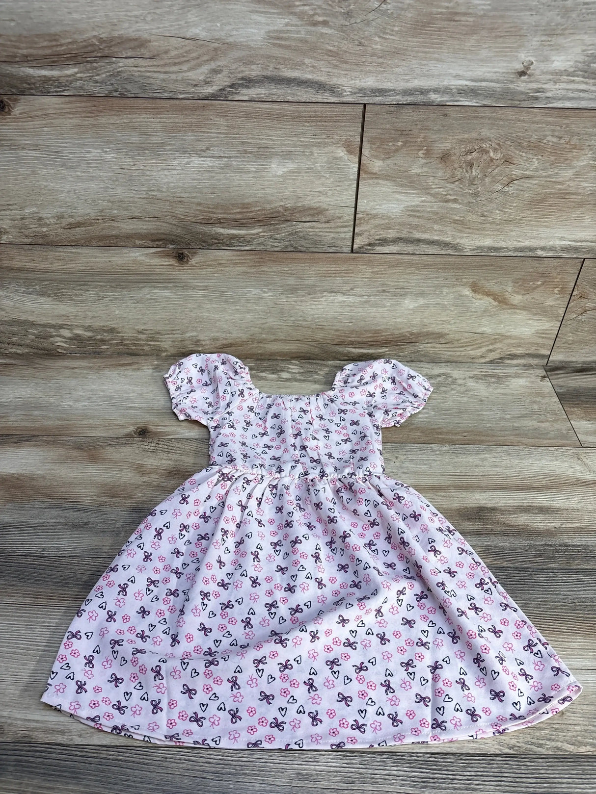 Flat lay of pink smocked floral toddler dress with smocked bodice, puff sleeves and gathered skirt on wood floor