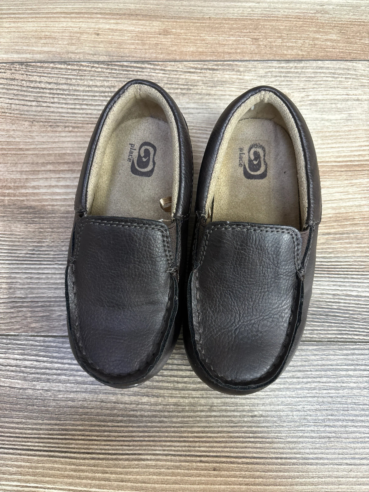 Pair of brown leather slip-on kids loafers on a wooden floor