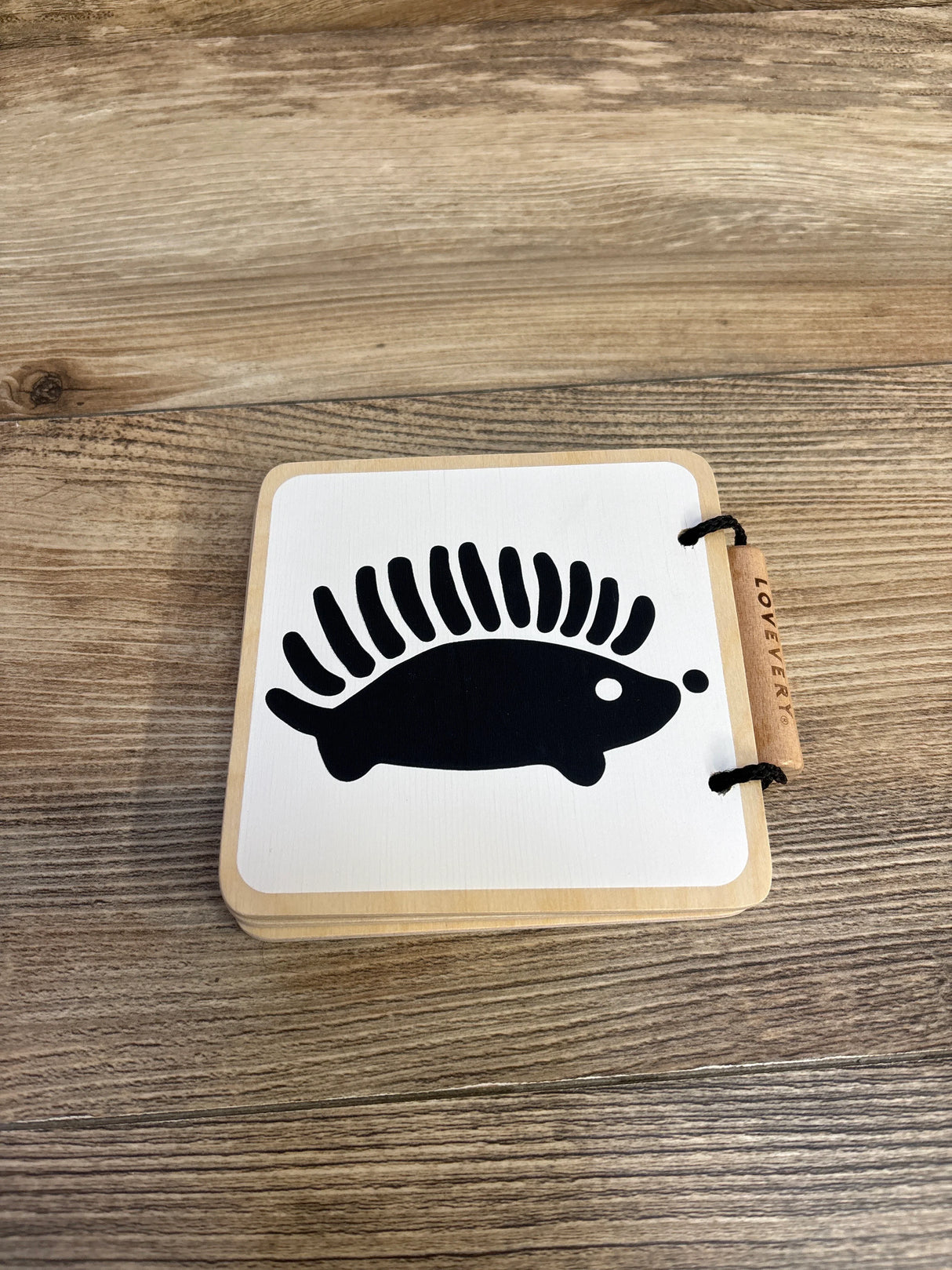Wooden flashcard with black hedgehog silhouette on white, on wood grain surface