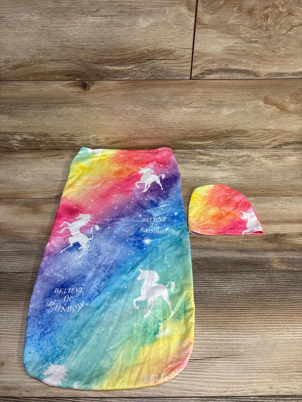 Colorful rainbow baby swaddle and matching hat with white unicorns and 'Believe in Rainbow' text