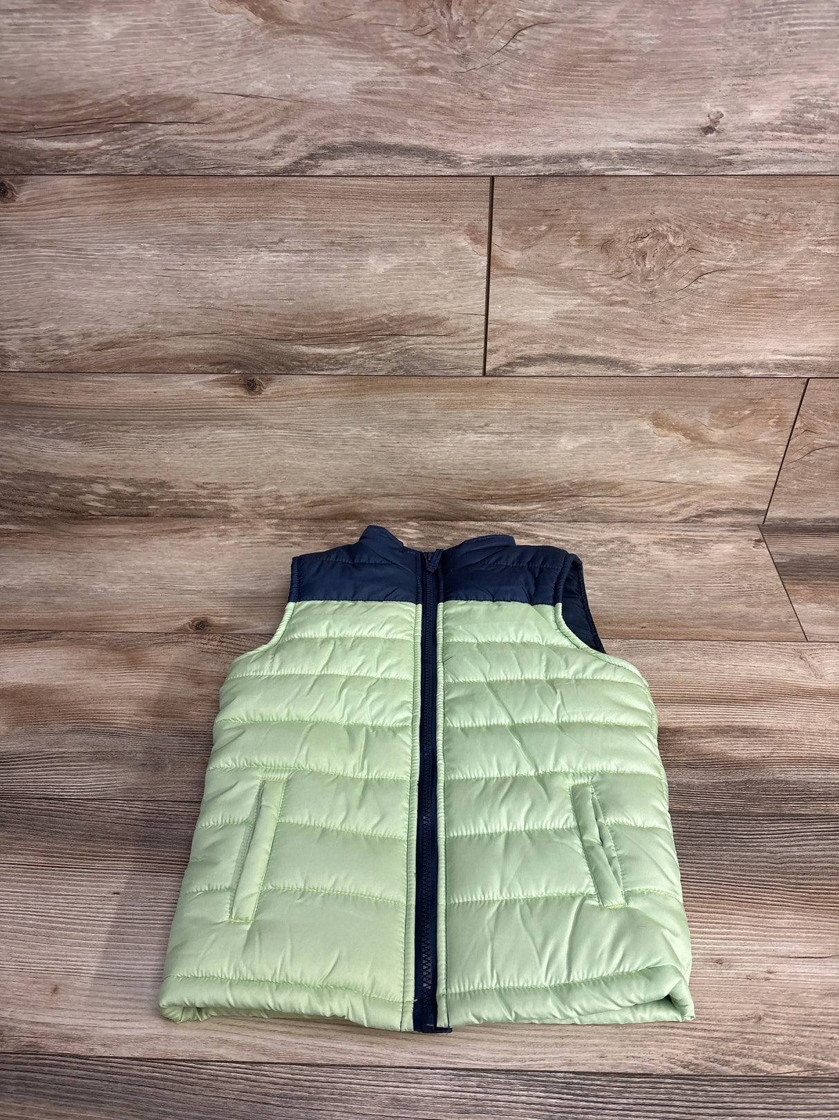 Front flat lay of Liberty Valor full-zip vest 4T showing light green body, navy collar and zipper on wood background