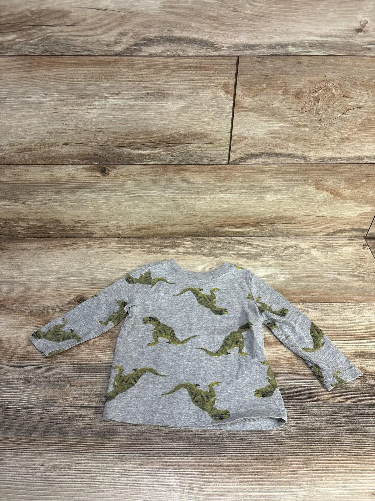 Flat lay of grey Old Navy long-sleeve toddler shirt showcasing green dinosaur print on wood background