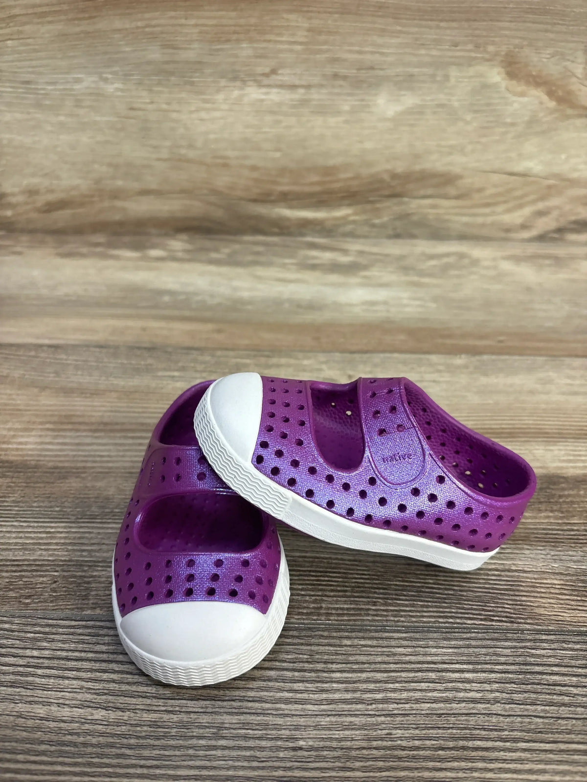 Angled view of Native Jefferson Juniper toddler shoes in purple showing perforated upper and white rubber toe and sole on wood background