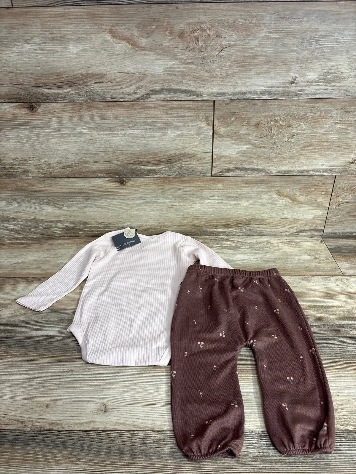 Top-down view of pink ribbed long sleeve bodysuit and brown patterned pants set on a wood-look floor