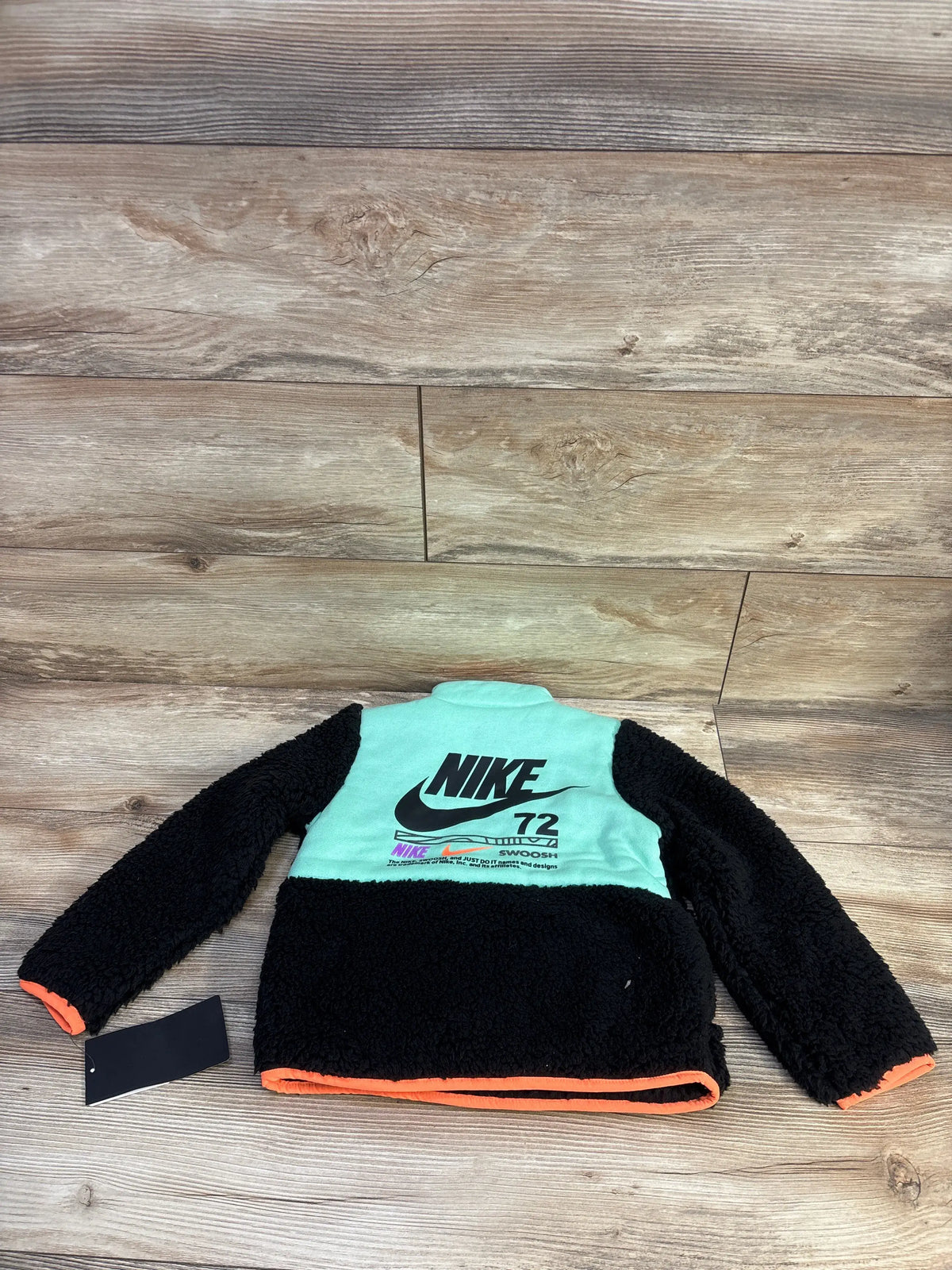 Back of Nike Sherpa jacket with mint upper panel and black NIKE logo, black sherpa body and orange trim on wood background