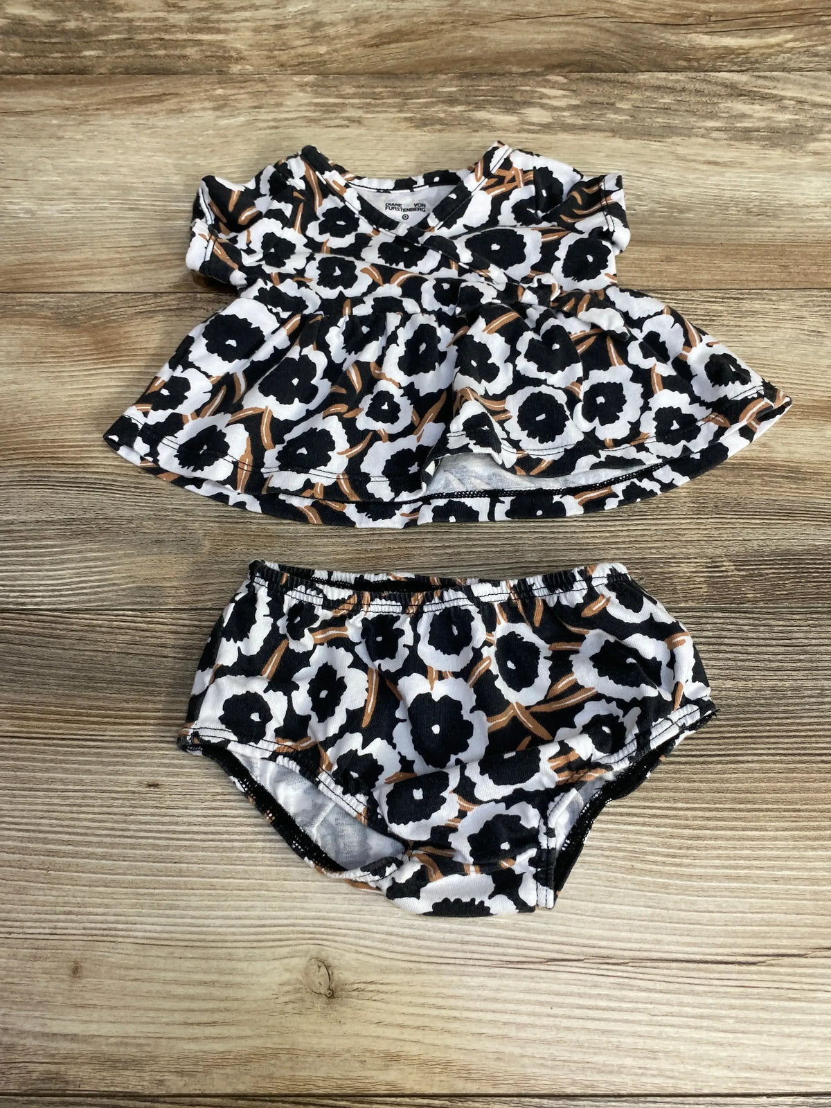 Flat lay of Diane Von Furstenberg baby faux-wrap top and matching bloomers in black, white, and tan floral on wood background