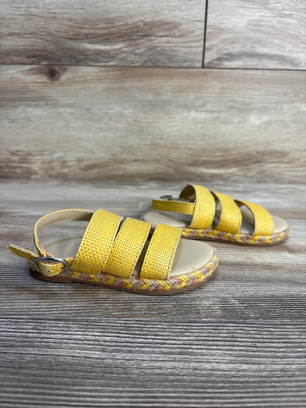 Yellow woven toddler sandals with buckles, open toe, and braided soles on wood background