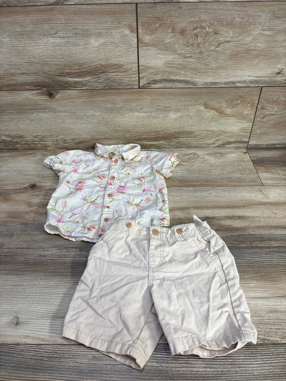 Top-down view of H&M button-up shirt and shorts set showcasing floral-print short-sleeve shirt and ivory shorts on wood floor