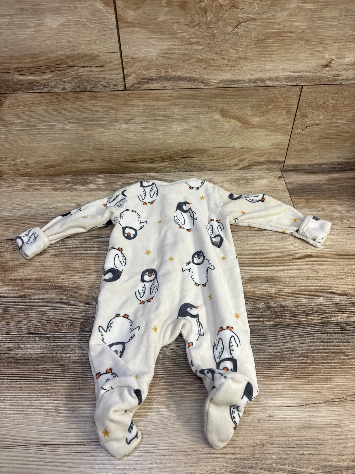 Top view of an ivory Old Navy penguin-print blanket sleeper with long sleeves and footed legs on a wood floor