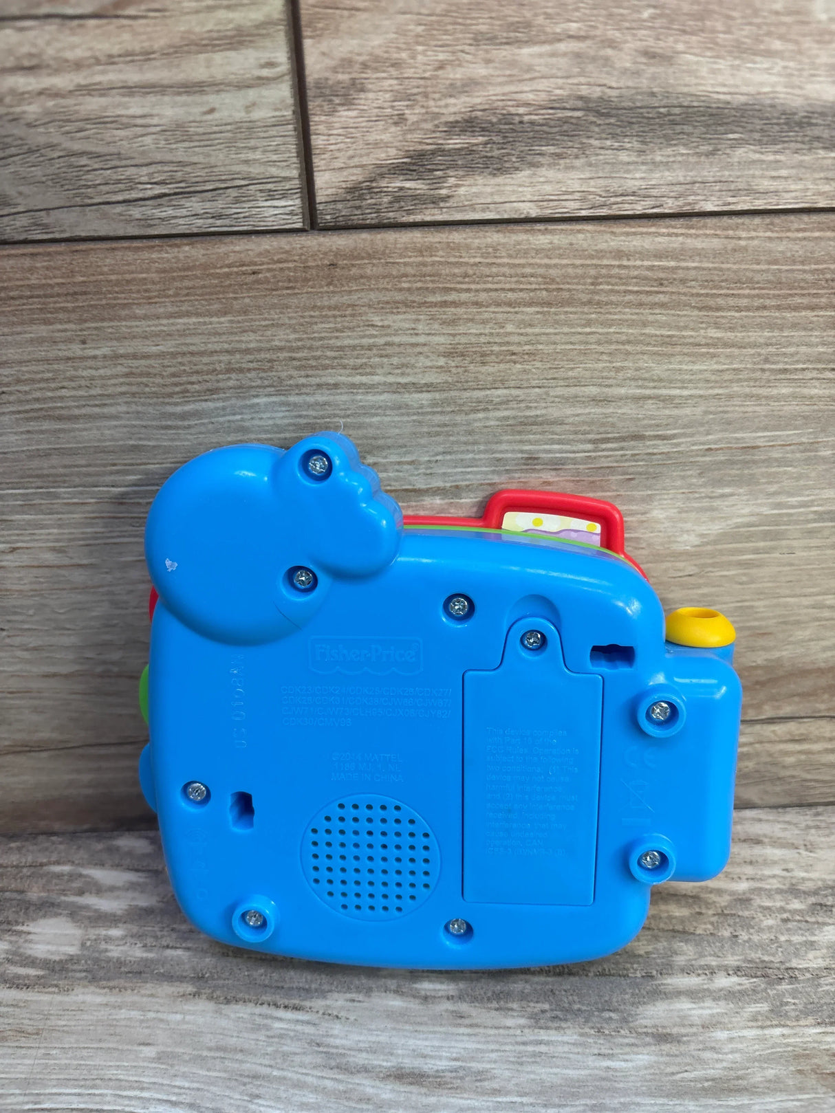 Rear view of Fisher-Price Counting with Puppy electronic book showing blue plastic back, speaker grille, battery compartment and screws on wood surface