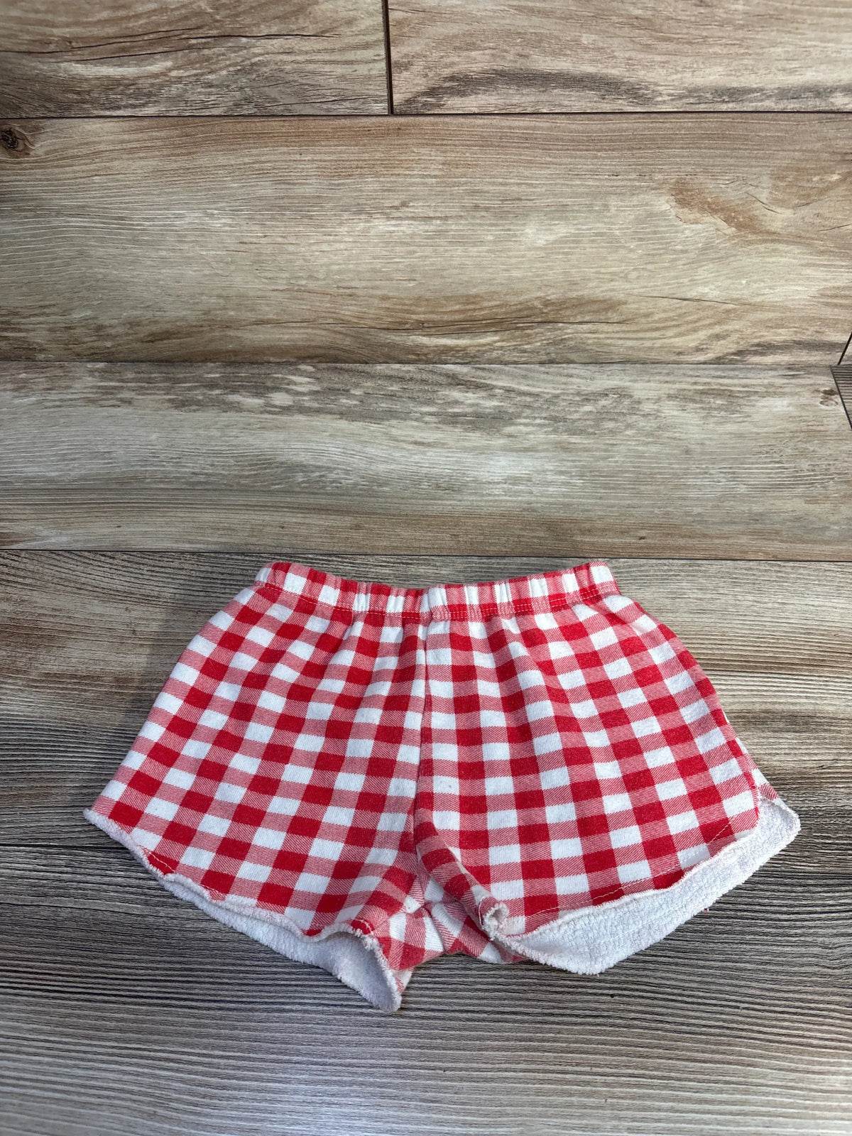 Top view of Grayson Mini checker shorts in red showcasing elastic waistband and relaxed fit on a wood background