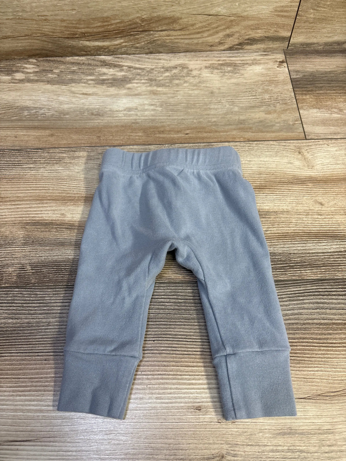 Front view of Little One Shop blue pull-on pants, size 3 months, showcasing elastic waist and ribbed cuffs on a wood floor