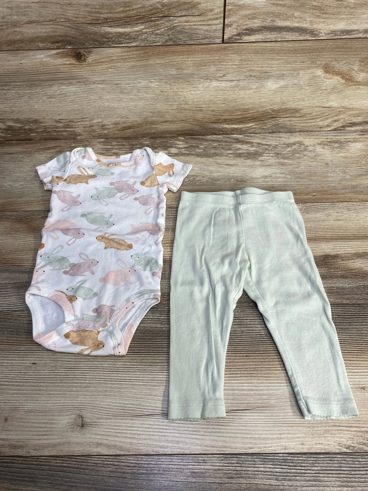 Flat lay of Carter's white baby bodysuit with pastel bunny print and pale green pants, snaps and elastic waist, on wood background