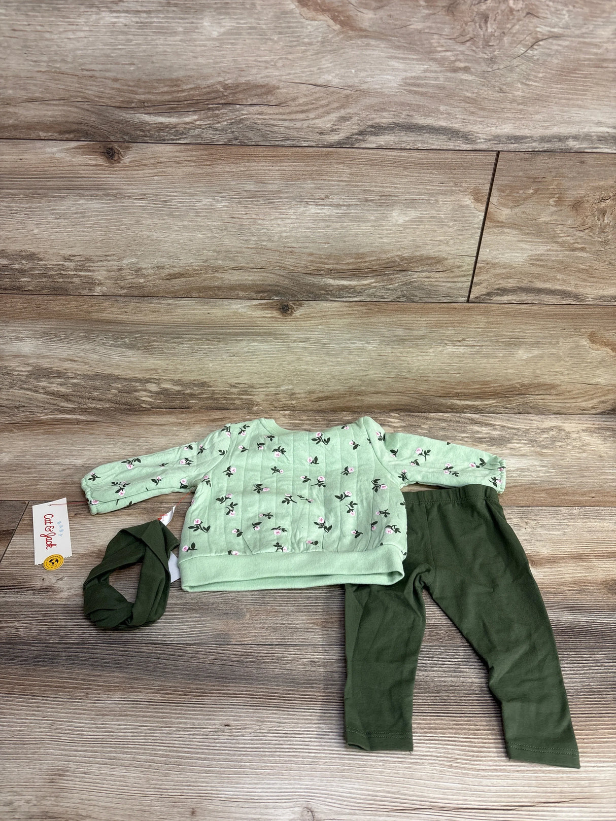 Light green floral baby sweater with matching headband and dark green leggings on wood floor