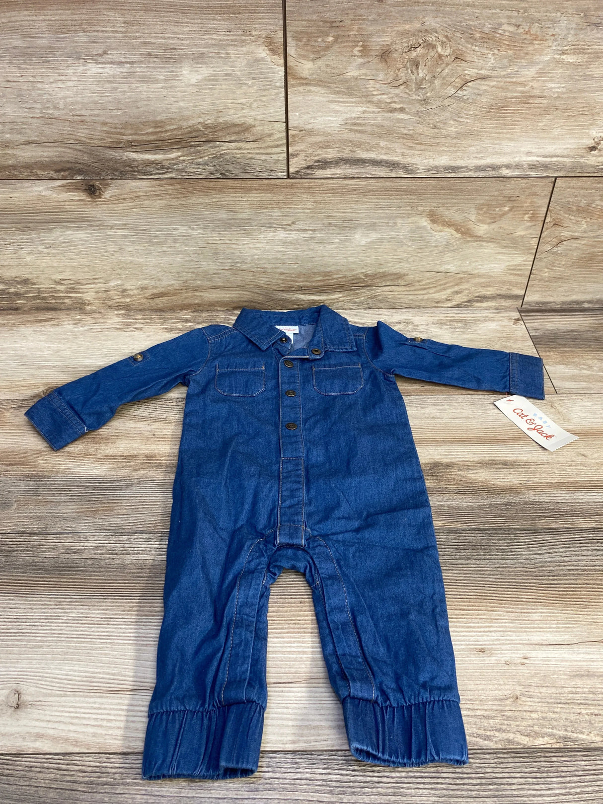 Blue denim baby romper with long sleeves and button details, laid flat on wooden floor
