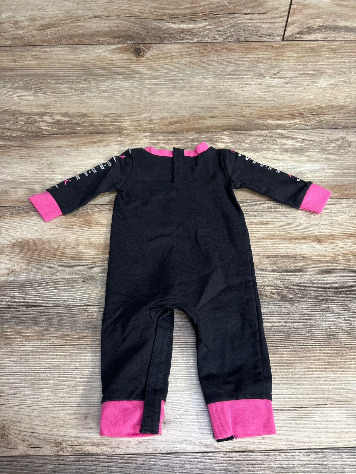 Black and pink long-sleeve infant romper with Jordan logo on wooden floor, kids clothes resale