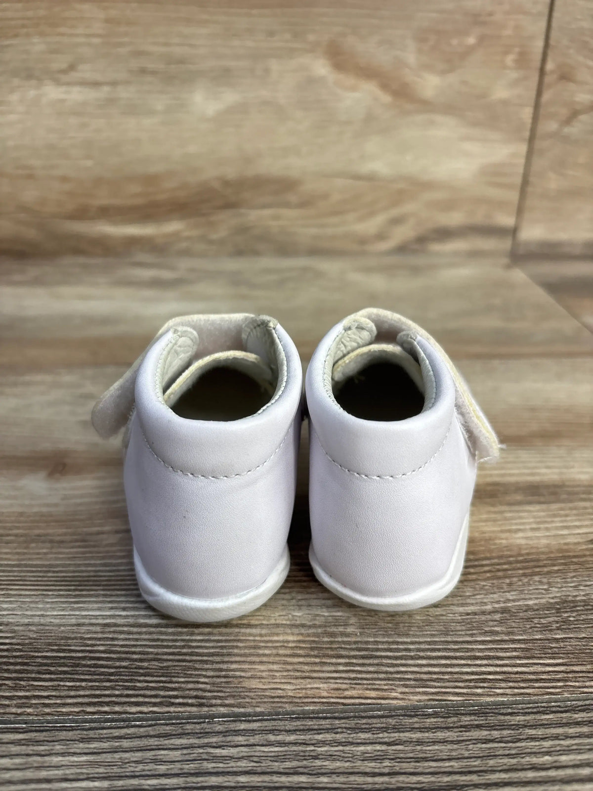 Rear view of white Alegria Kids patent leather first walker shoes on a wooden surface.