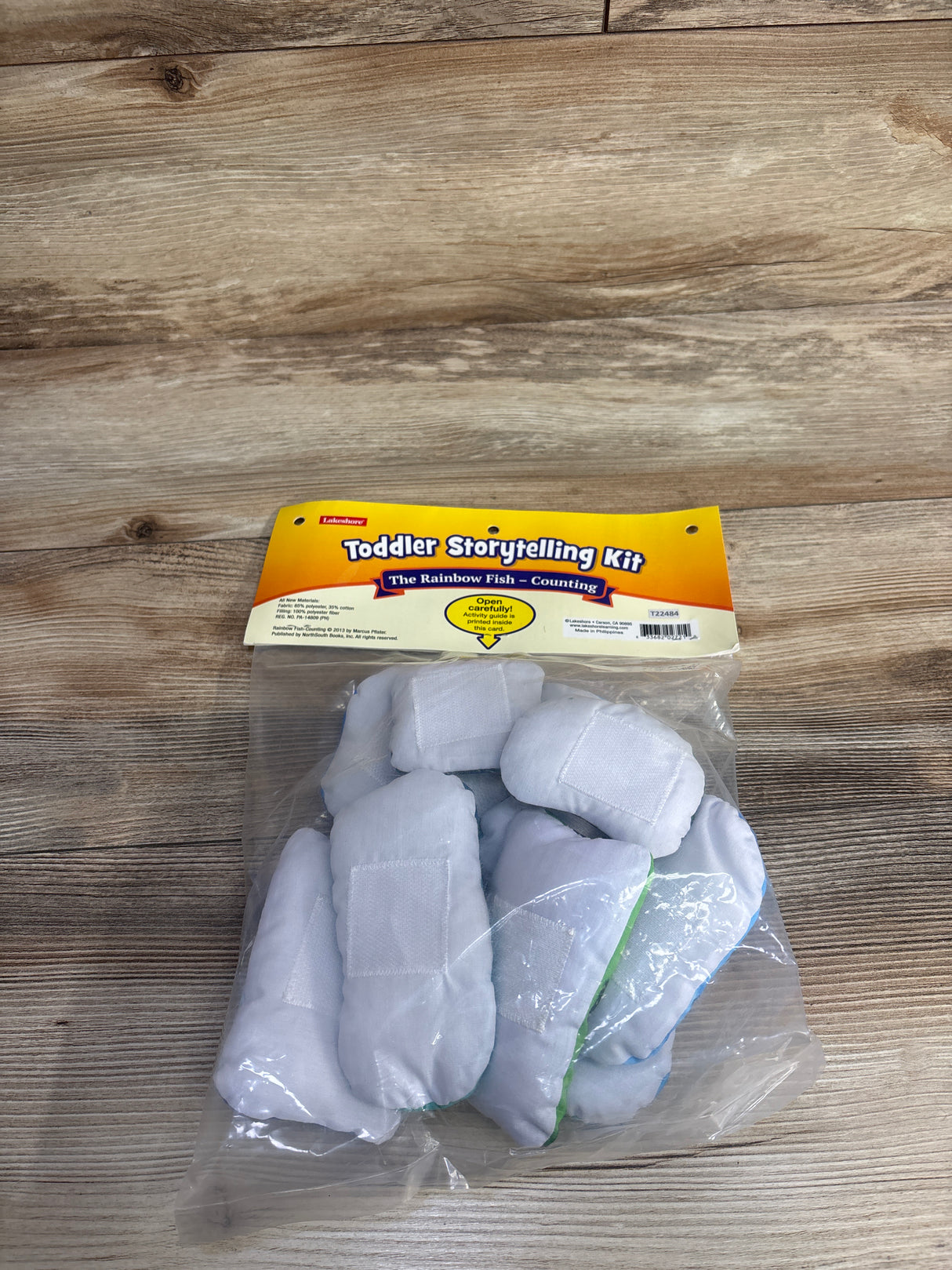 Toddler Storytelling Kit The Rainbow Fish Counting with soft fabric fish pieces in plastic bag on wood surface