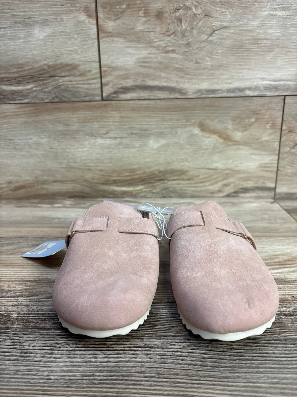 Pair of pink suede slip-on shoes with white sole on a wooden surface, children's footwear