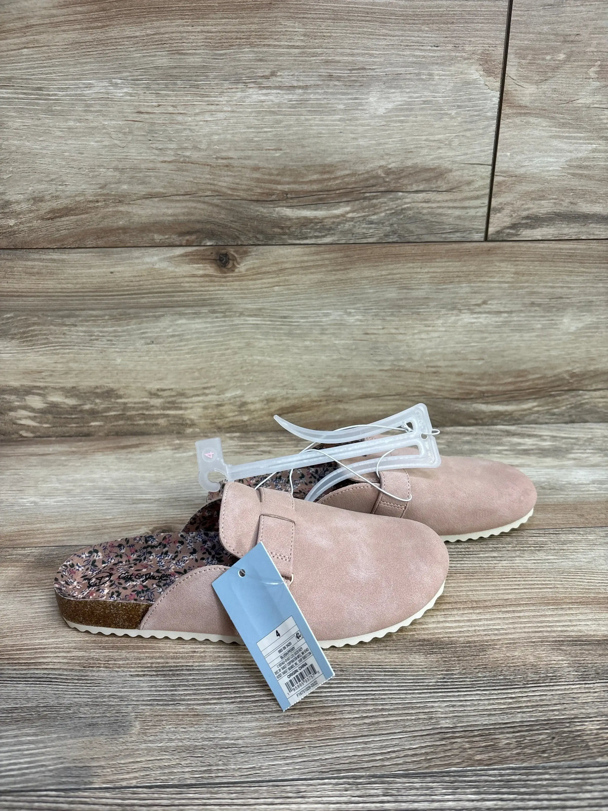Pink slip-on shoes with floral insole and tags, displayed on wooden background