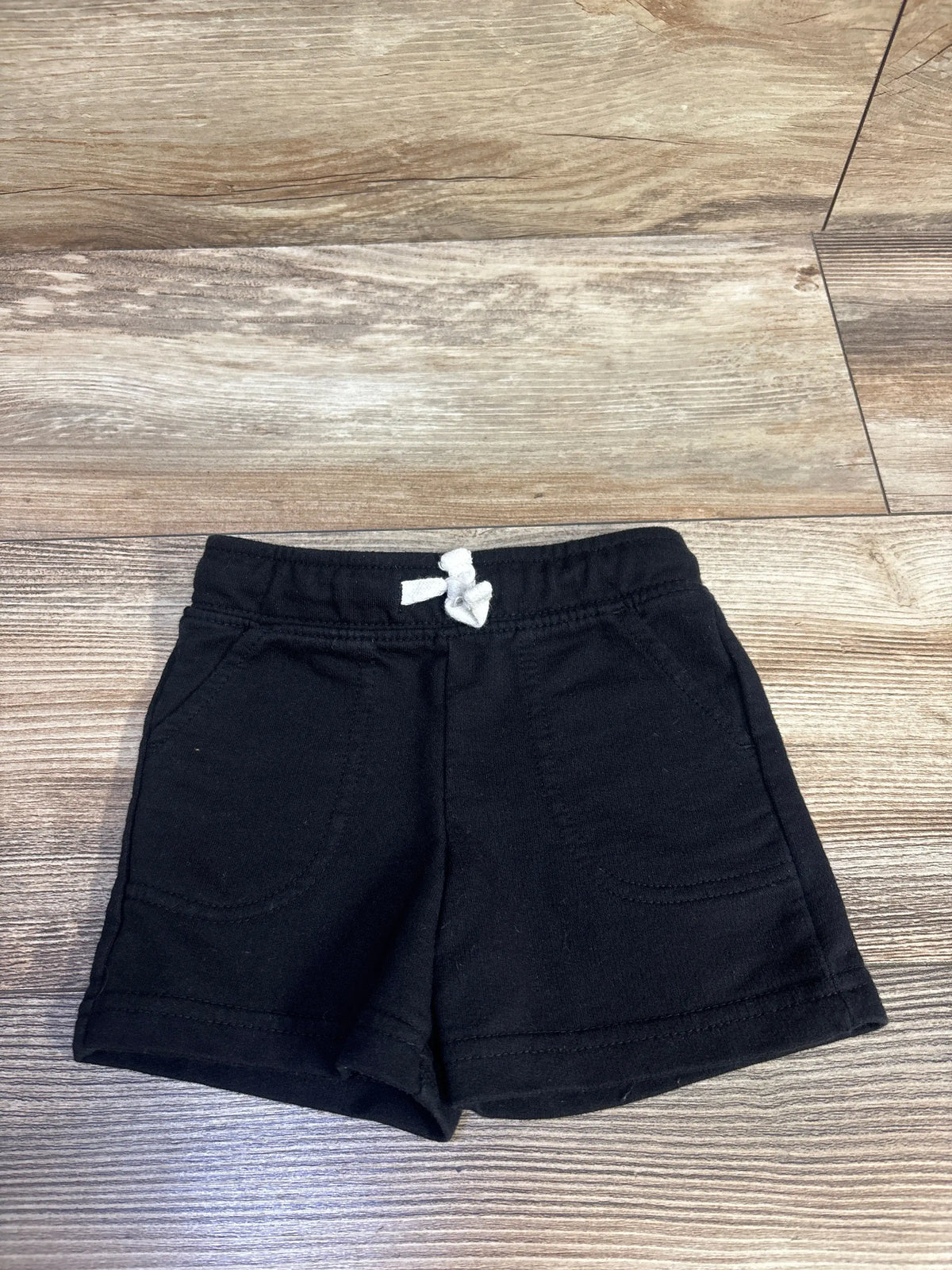 Cat & Jack black drawstring shorts for baby size 12m on a wooden surface