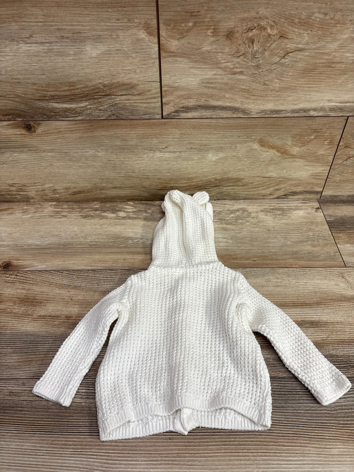 Back view of Carter’s white knit hooded sweater with long sleeves and ribbed hem on a wood floor