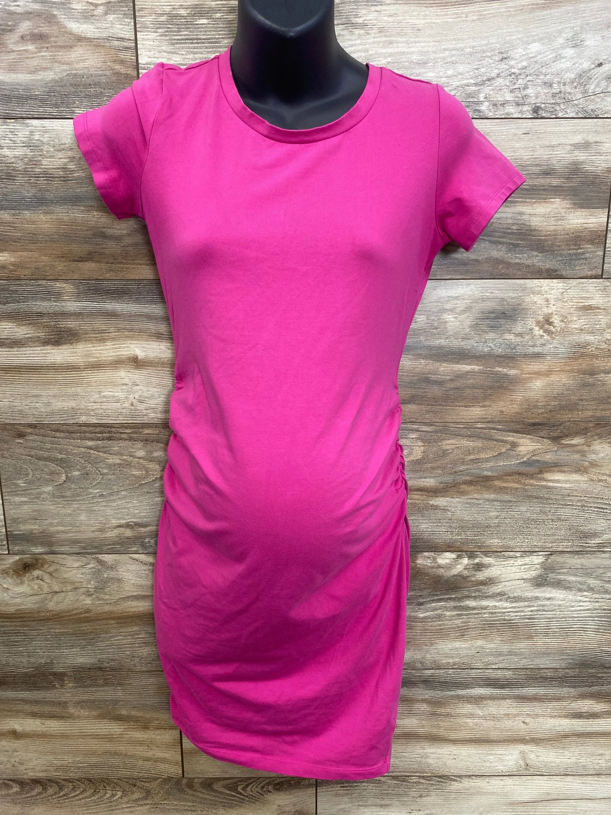 Bright pink maternity t-shirt with ruched side panels, displayed on mannequin against wood background