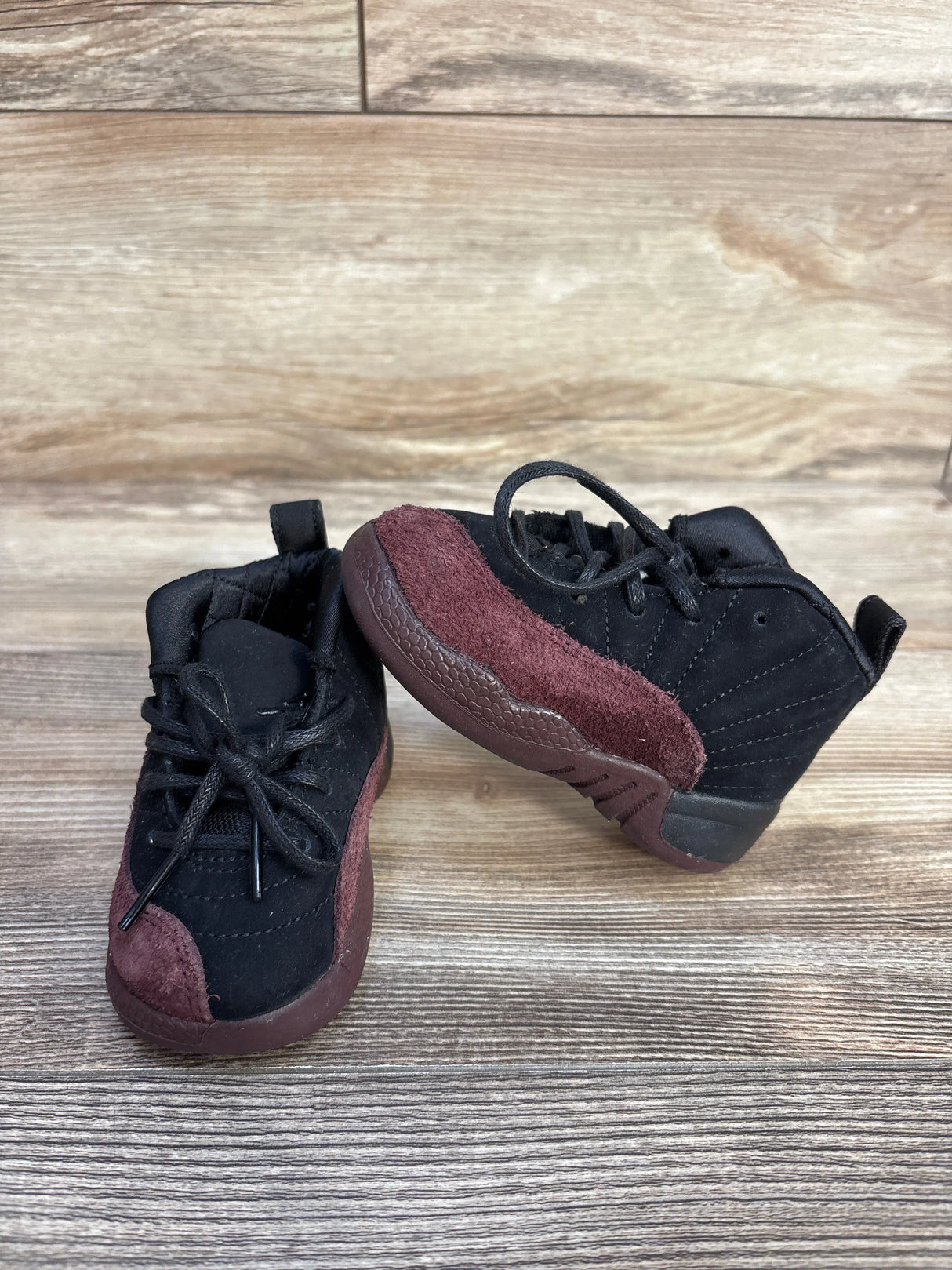 Black and maroon toddler sneakers with suede details on wood floor