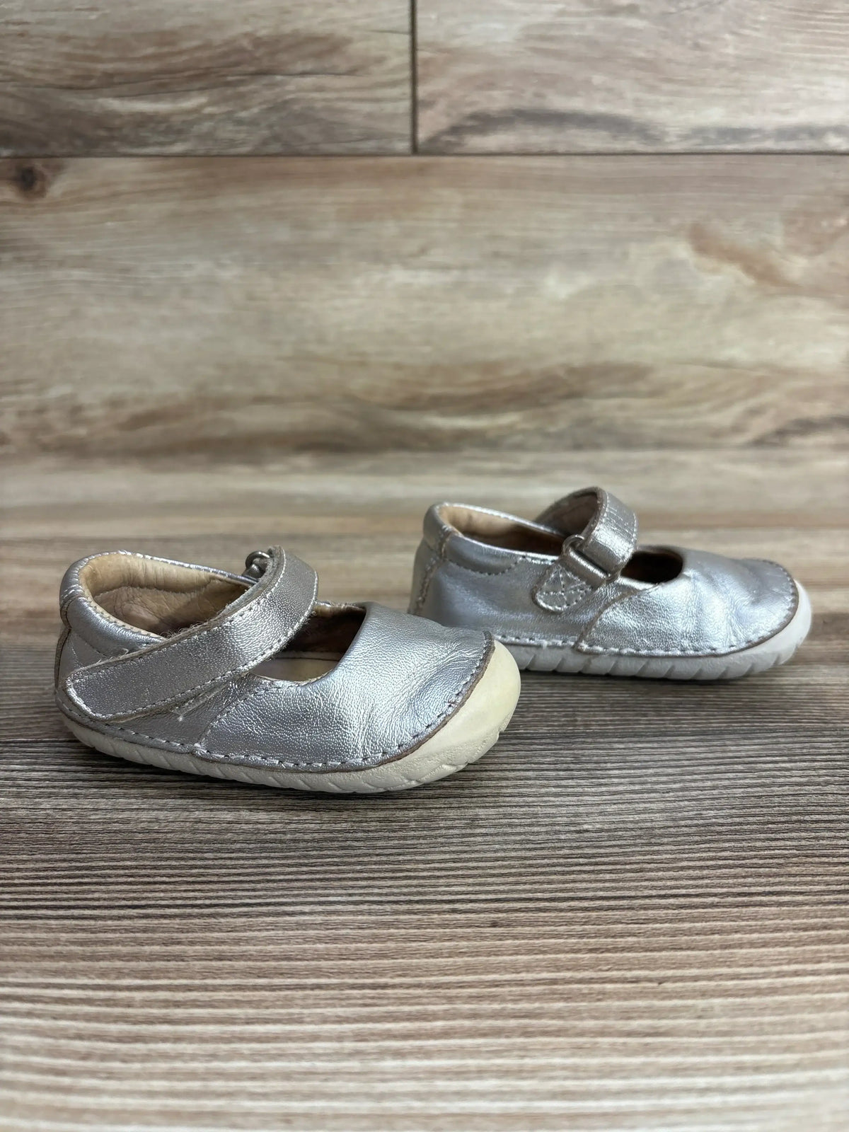Pair of silver toddler Mary Jane shoes with velcro straps on wooden floor