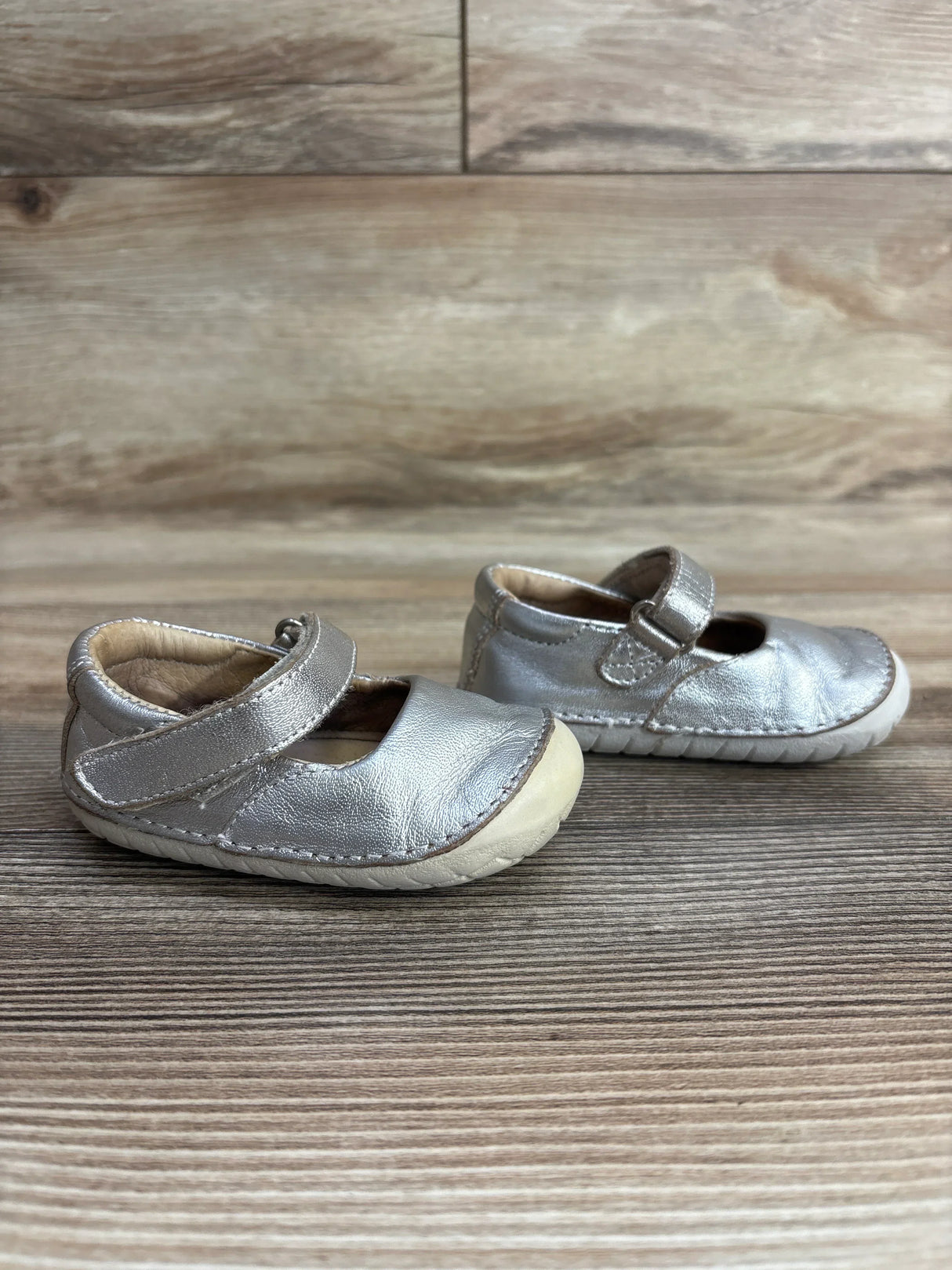 Pair of silver toddler Mary Jane shoes with velcro straps on wooden floor