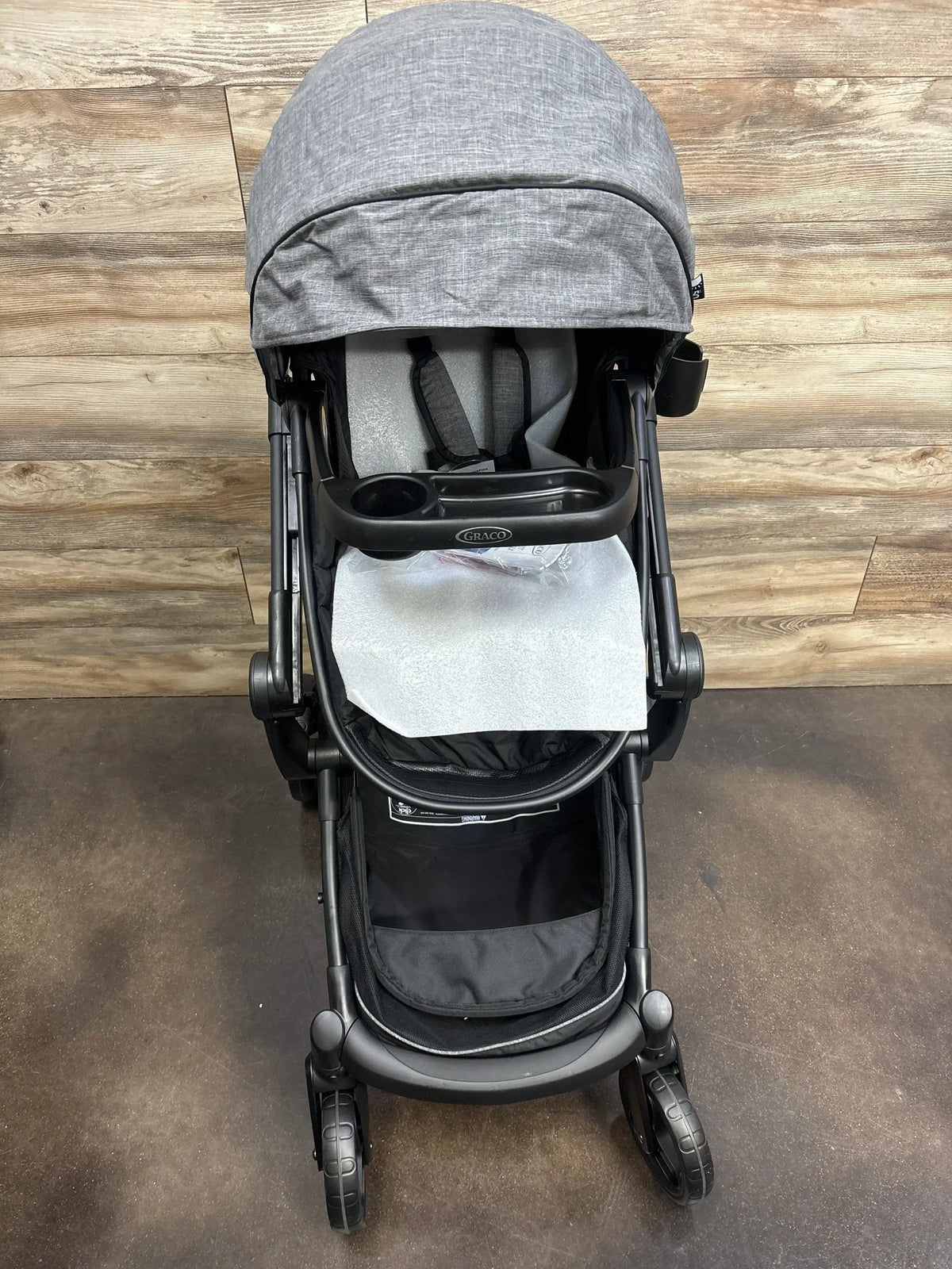 Gray Graco baby stroller with canopy, cup holder, and storage basket on wood floor
