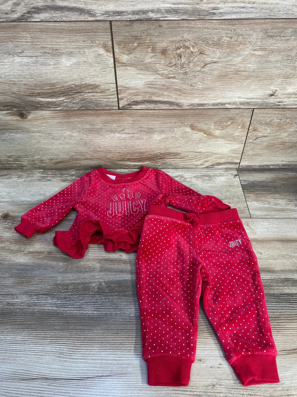 Top-down view of Juicy Couture red velvet sweatshirt and joggers set showcasing peplum hem and ribbed cuffs on wood planks