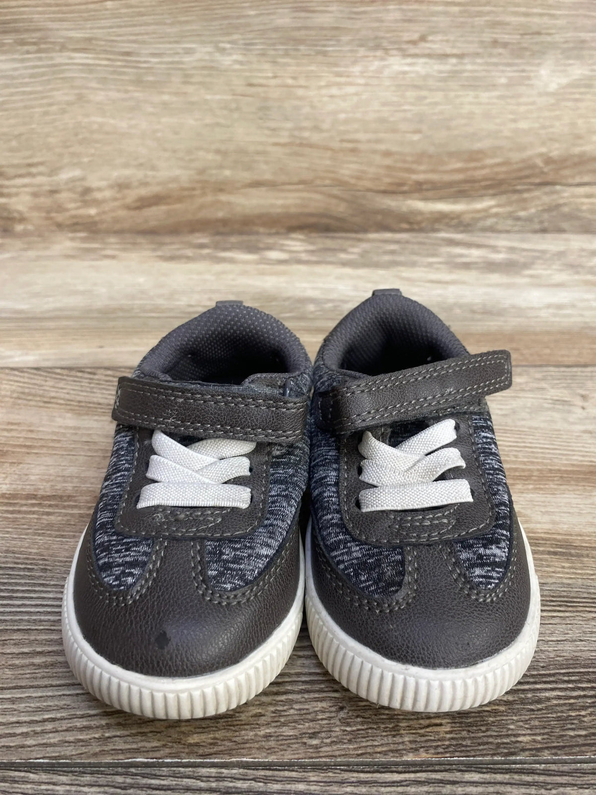 Pair of gray and white toddler sneakers with Velcro straps on wooden floor