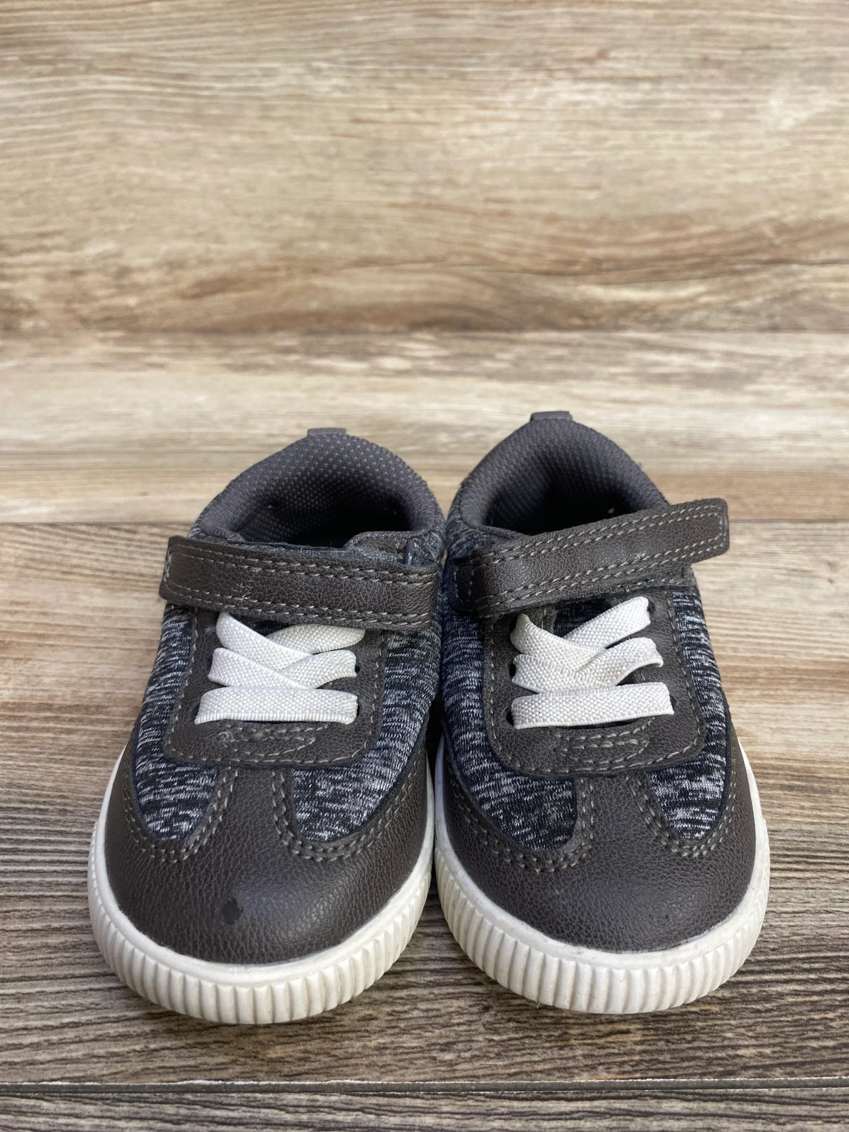 Pair of gray and white toddler sneakers with Velcro straps on wooden floor