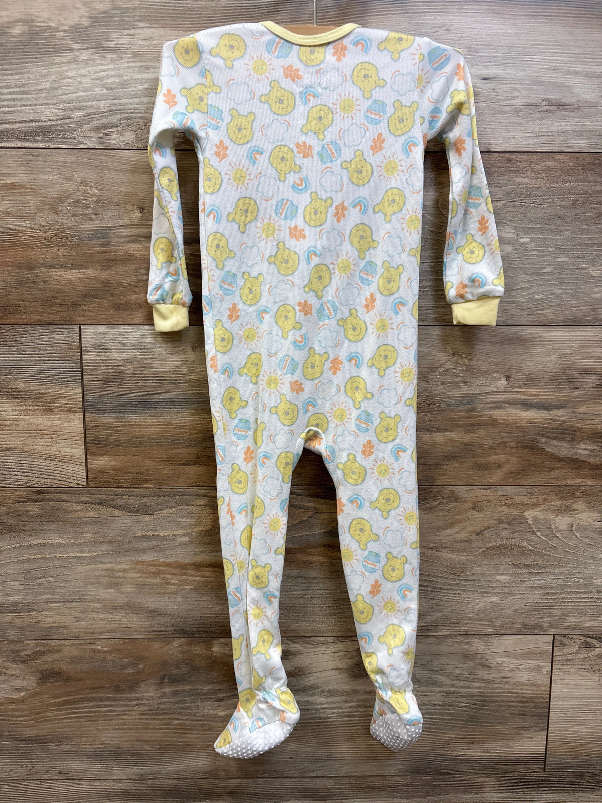 Front view of white Disney Baby Winnie the Pooh sleeper with full-length feet and character print on a wood floor