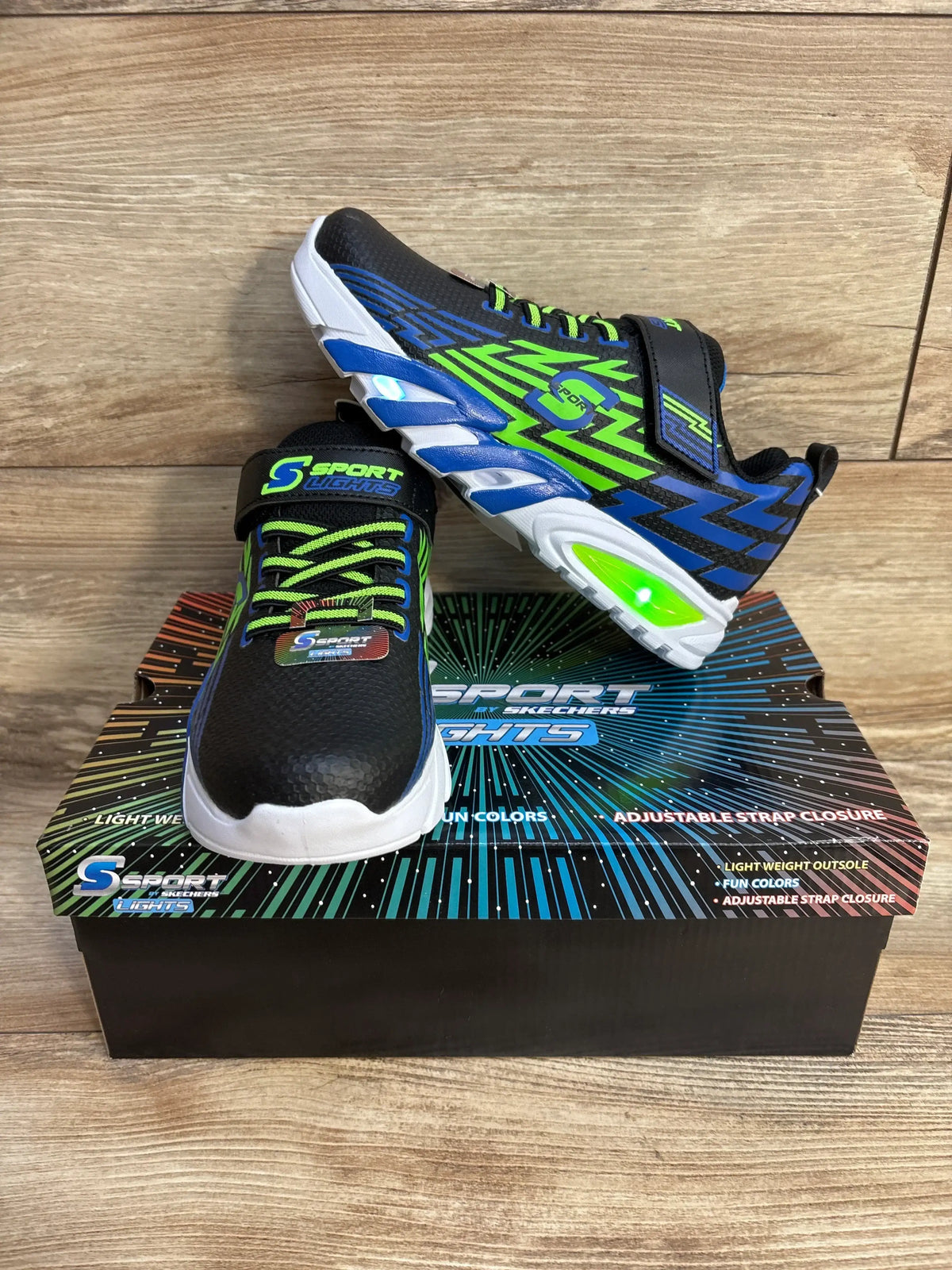Three-quarter view of kids’ Skechers S Sport Lights Ottis sneaker, black with blue and neon green accents and light-up sole
