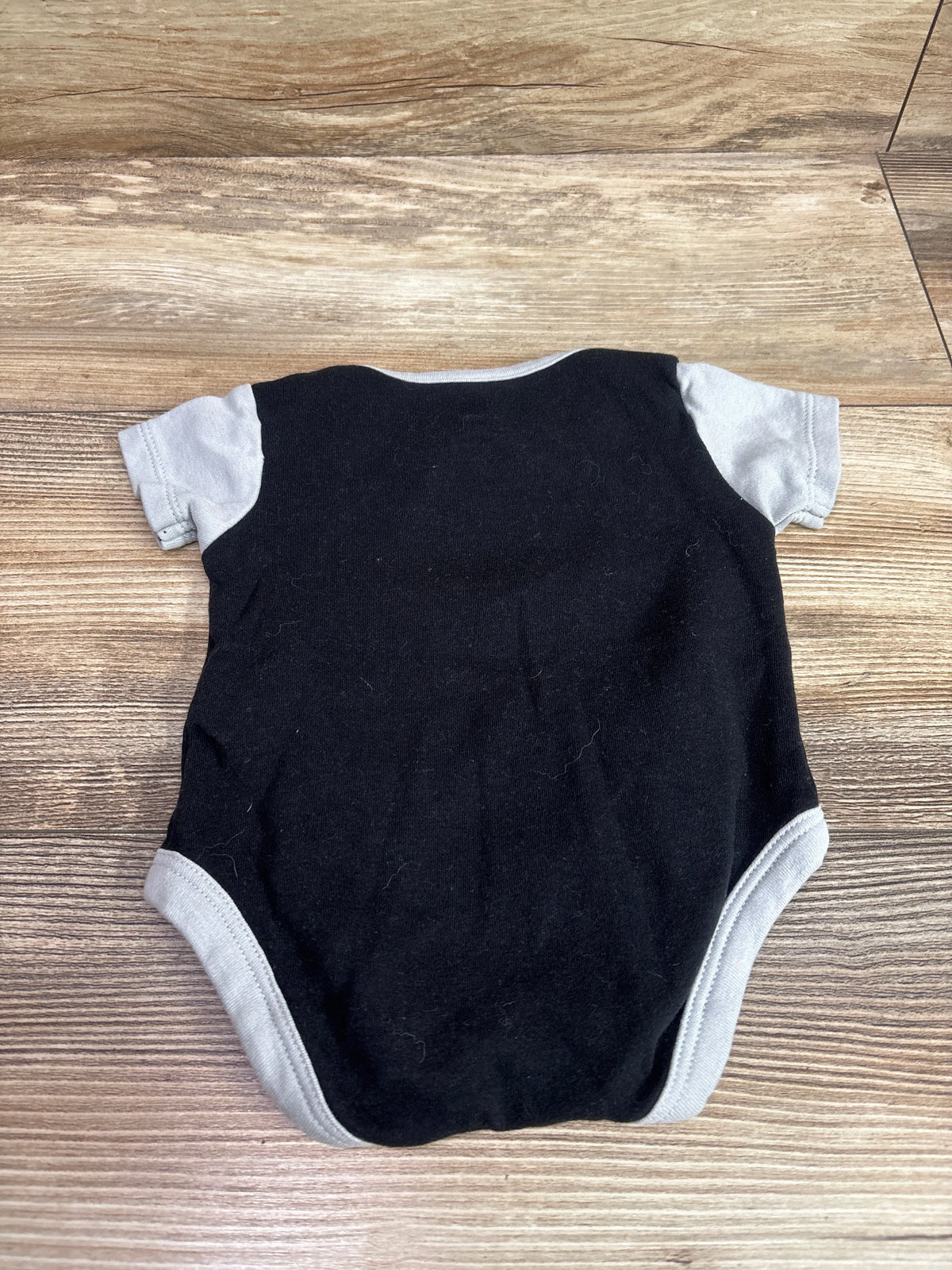 Back view of black Raiders bodysuit showcasing gray trim and short sleeves on a wood surface