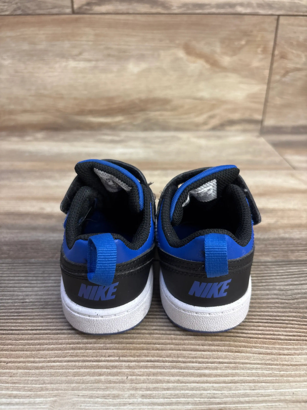 Rear view of Nike Court Borough Recraft TD sneakers showcasing Game Royal and black uppers, pull tabs, and white soles on a wood floor
