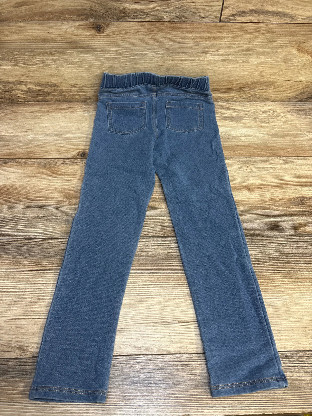 Back view of blue denim kids leggings with elastic waistband and pockets on wood floor