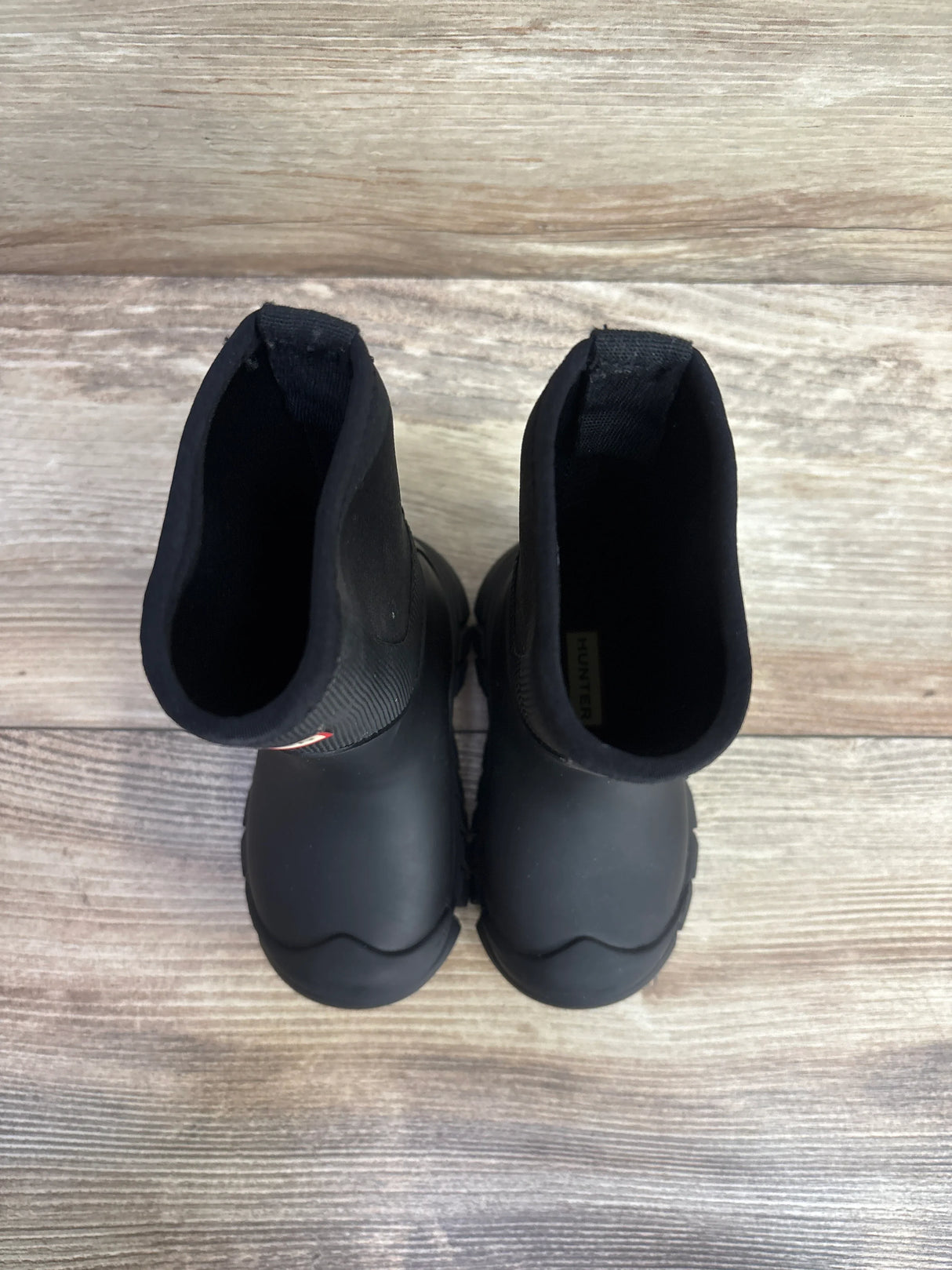 Pair of black children's rubber boots with pull-on design on wooden floor