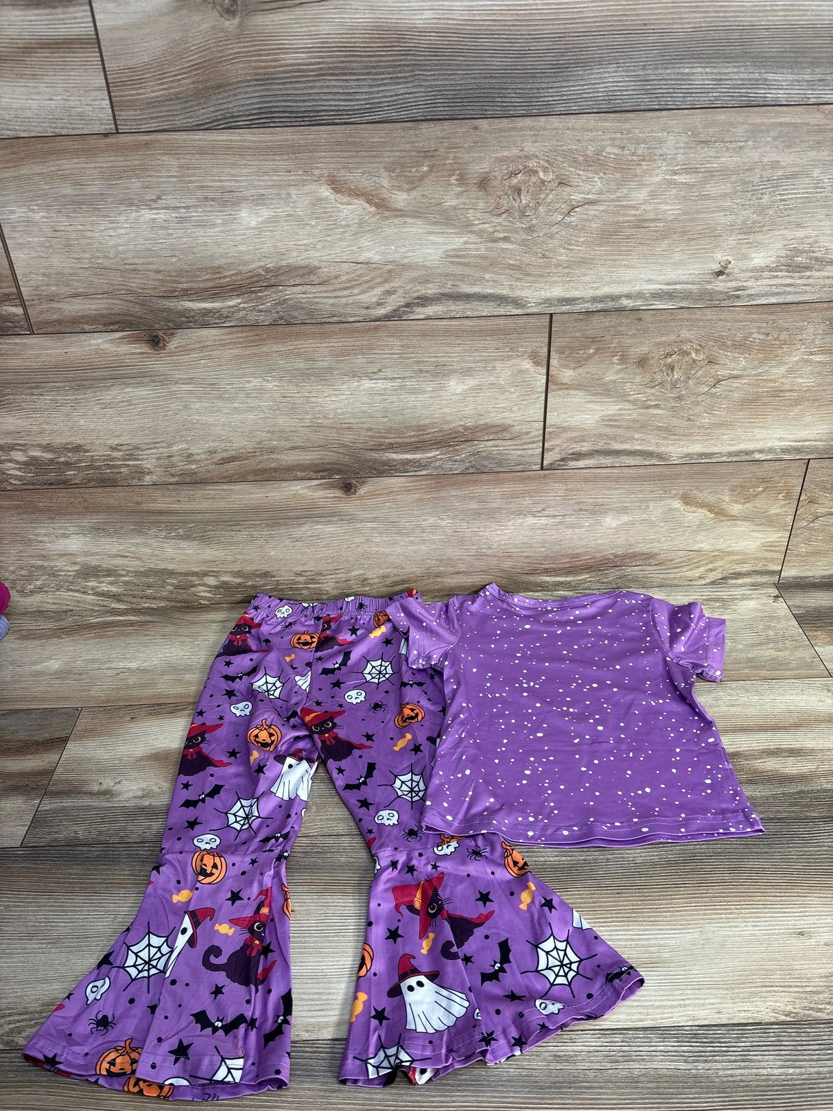 Purple Halloween-themed kids pajama set with witch, ghost, and pumpkin prints on wood floor