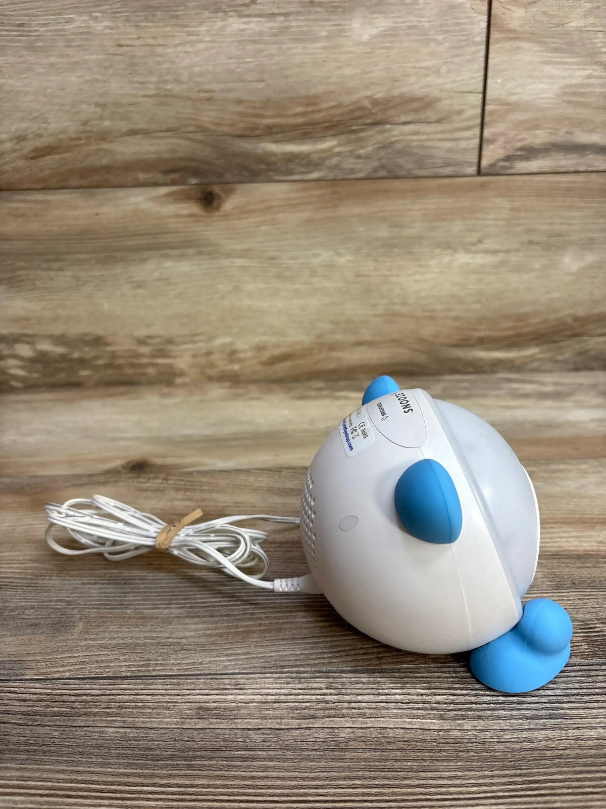 Side view of WindFlyer OK to Wake clock with white rounded body, blue buttons, and coiled power cord on wood background