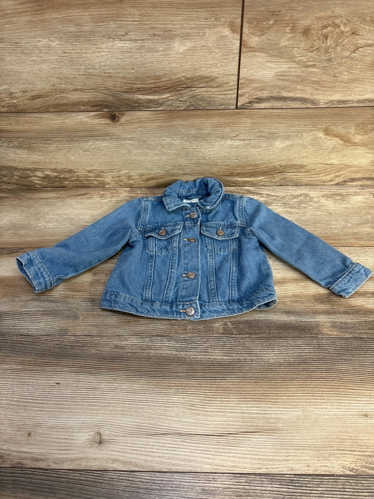 Front view of Baby Gap x Disney Minnie Mouse Icon denim jacket showcasing button front and chest flap pockets on a wood floor