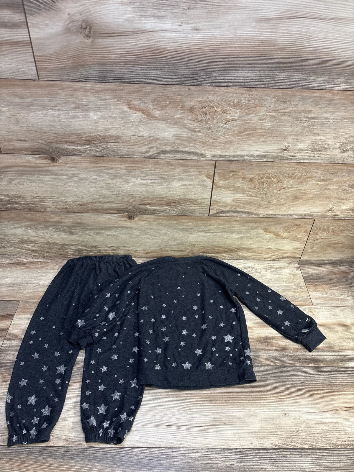 Flat lay of kids raglan pullover and pants set showing grey fabric with silver stars, elastic waist and cuffed ankles on wood floor
