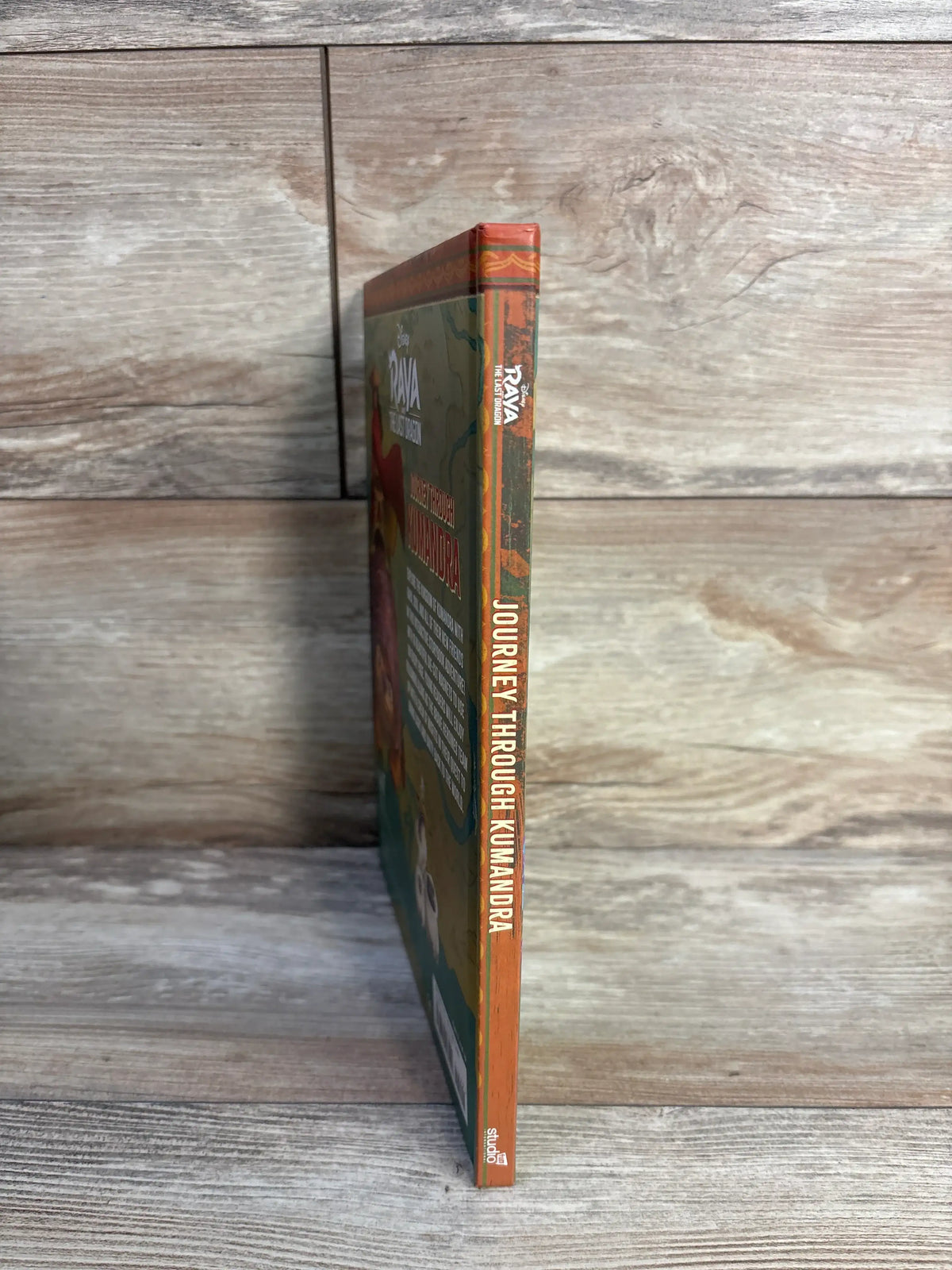 Side view of Raya and the Last Dragon magnetic hardcover book showcasing orange spine text on a wood surface