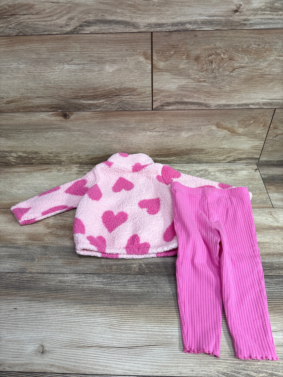 Flat lay of pink Just One You sherpa sweatshirt and pants set with heart pattern and ribbed pants on wood